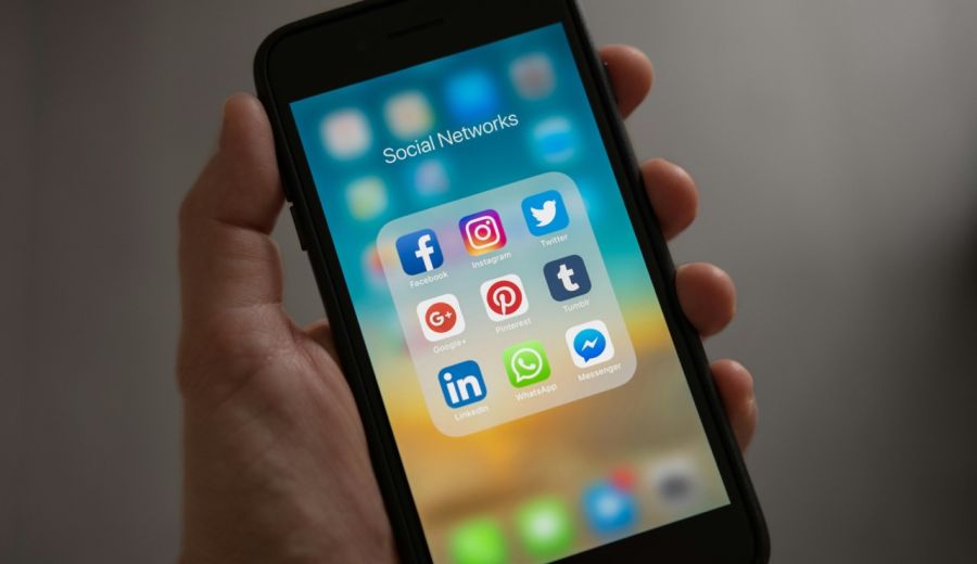 Eine Hand die ein altes iPhone hält, das Display zeigt den Home Bildschirm mit dem Ordner Social Networks geöffnet, darin befinden sich App Icons von Facebook, Instagram und mehr.