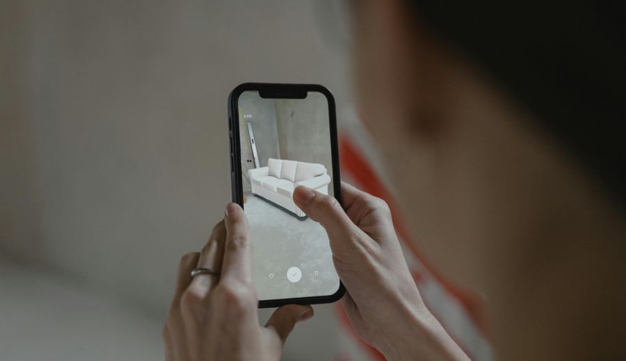 Eine Person hat ein Smartphone in der Hand und platziert auf dessen Display n in den Raum projeziertes Sofa. Bild Quelle: pexels.com